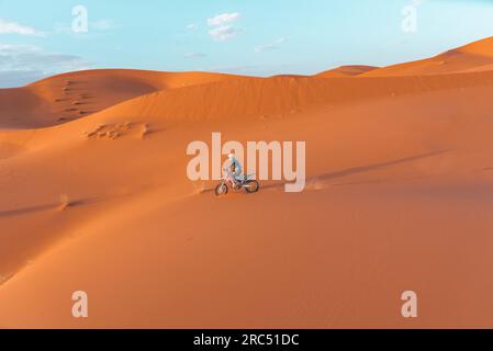 Seitenansicht einer nicht wiedererkennbaren Person, die Motorrad auf Sanddünen vor bewölktem Himmel in der Merzouga-Wüste Marokko fährt Stockfoto