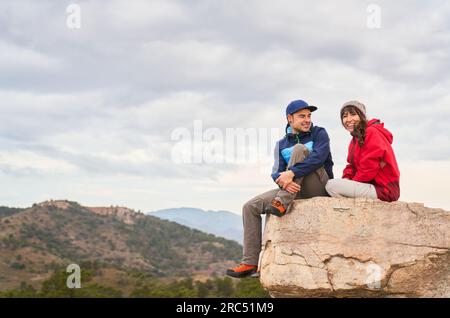 Fröhliche Ehefrau und Ehemann sittinf auf dem Gipfel des Berges und genießen die majestätische Landschaft des Hochlands in Spanien Stockfoto