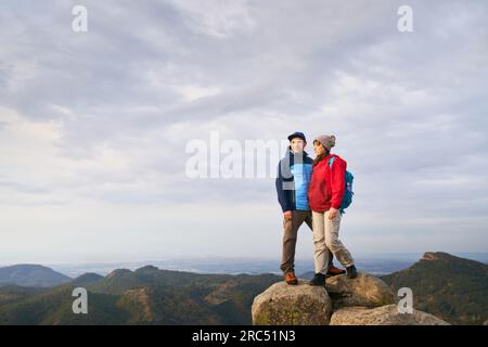 Ehefrau mit Rucksack mit Ehemann auf dem Gipfel des Berges und genießen die majestätische Landschaft des Hochlands in Spanien Stockfoto