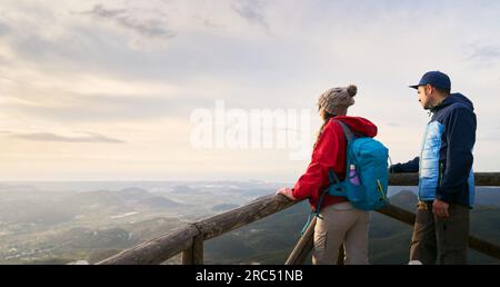 Seitlicher Blick auf Freund und Freundin mit Rucksack auf dem Gipfel des Berges, die Landschaft des Tals bei Sonnenuntergang in Spanien genießen Stockfoto