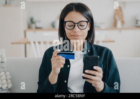 Fokussierte Frau kauft online ein und zahlt mit der mobilen Banking-App. Kreditkarte und Smartphone in der Hand. Komfort beim E-Banking. Stockfoto