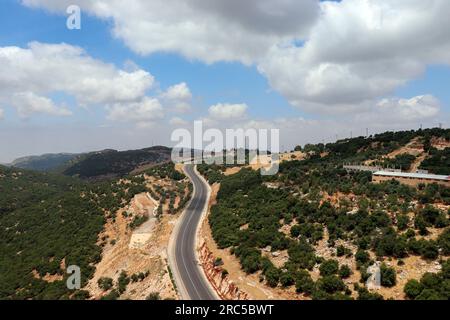 Lange Fahrt auf Autobahnen zwischen Städten (Straße, Wälder, Berge, Wolken und grüne Bäume in Ajloun, Jordanien), ein Luftblick von der Seilbahn Stockfoto