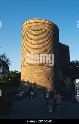 Baku, Aserbaidschan - 25. Juni 2023: Der historische Jungfernturm tauchte im warmen Licht des Sonnenuntergangs auf, mit Touristen im Vordergrund Stockfoto