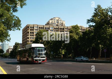 Baku, Aserbaidschan - 26. Juni 2023: Ein vorbeifahrender Bus auf den Straßen von Baku, mit einem historischen Gebäude in der Nähe des Regierungsgebäudes im Hintergrund Stockfoto
