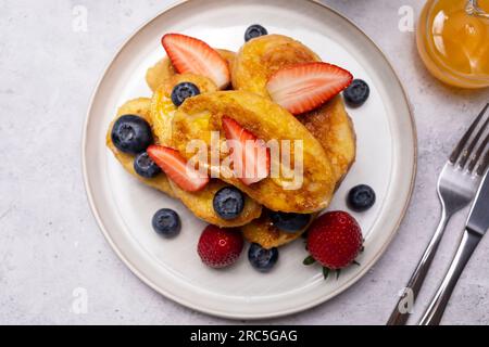 Torrijas, Französischer Toast Im Spanischen Stil Mit Orangengarnierung, Glasur, Frischen Blaubeeren, Erdbeere Auf Grünem Teller, Holztisch. Eine Hälfte Orange Stockfoto