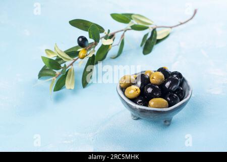 Schwarze und grüne griechische Oliven in einer Schüssel auf blauem, sonnigen Hintergrund. Speicherplatz kopieren Stockfoto