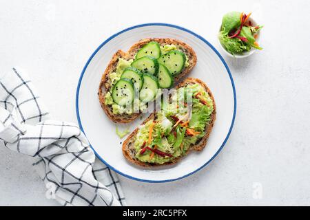 Vegane Avocado-Toasts mit Garnierung aus Gurken und frischem grünen Salat mit geriebener Karotte und roher Rüben. Sauberes Essen, Diätkonzept. Draufsicht Stockfoto