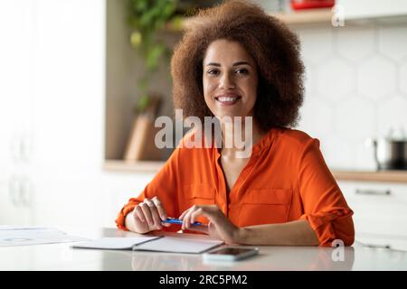 Wunderschöne, Lächelnde Junge Schwarze Frau Sitzt Am Tisch In Der Küche Stockfoto