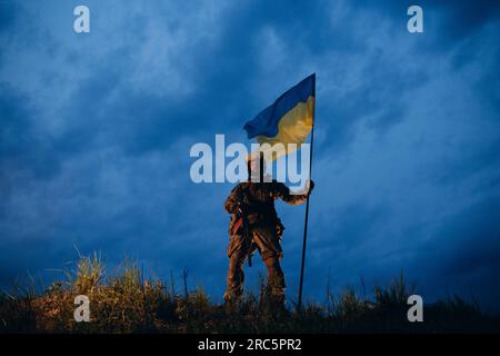 Bewaffneter ukrainischer Krieger mit blauer und gelber Flagge am Abend Stockfoto