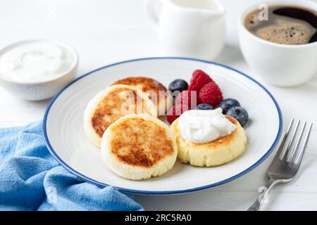 Hüttenkäse, Frittierte Syrniki Mit Beeren, Sour Cream Und Eine Tasse Schwarzen Kaffee Stockfoto