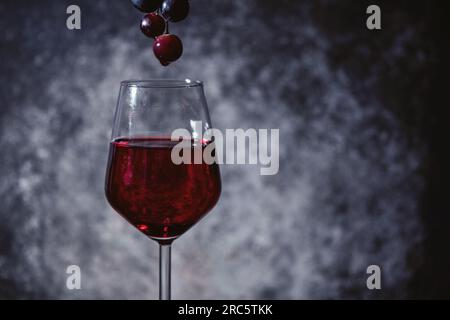 Rote Trauben mit Rotweinglas auf Holzhintergrund, Nahaufnahme, Makrofotografie, Details Stockfoto