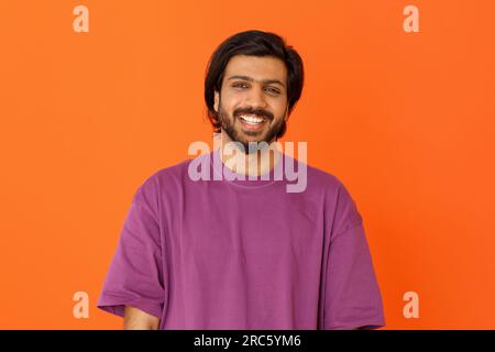 Fröhlicher, positiver, gutaussehender Ost-Typ, der auf orangefarbenem Hintergrund Stockfoto