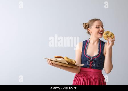 Wunderschöne Oktoberfest-Kellnerin mit Snacks auf hellem Hintergrund Stockfoto