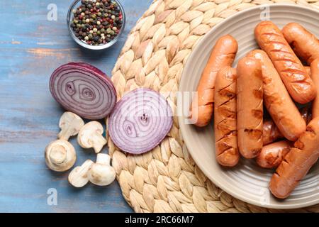 Teller mit leckeren Würstchen, Zwiebeln und Pilzen auf blauem Holztisch Stockfoto