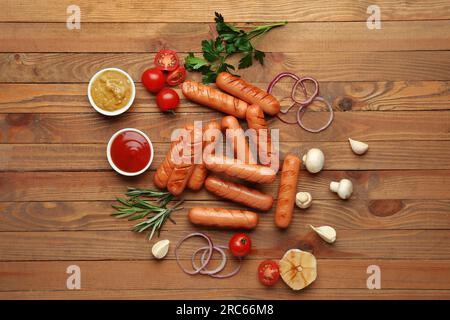 Leckere gegrillte Würste, Gemüse, Kräuter und Soßen auf einem Holztisch Stockfoto