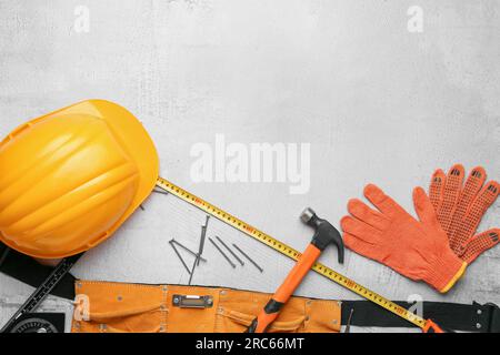 Werkzeuggürtel mit Hammer, Schutzhelm, Handschuhen und Nägeln auf grauem Hintergrund. Feierlichkeiten zum Labor Day Stockfoto