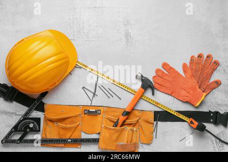 Werkzeuggürtel mit Hammer, Schutzhelm, Handschuhen und Nägeln auf grauem Hintergrund. Feierlichkeiten zum Labor Day Stockfoto