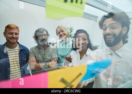 Gruppe fröhlicher Mitarbeiter, die sich zur Strategiekonferenz mit Brainstorming treffen und sich im Büro Notizen machen Stockfoto