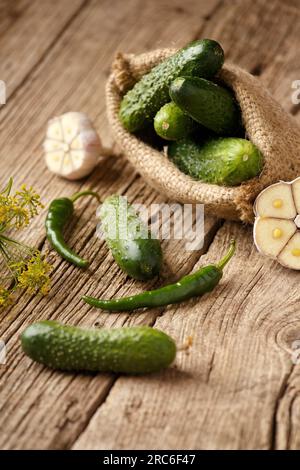 Frische Gurken in Leinenrot, Knoblauch und Paprika auf einem alten Holzhintergrund. Bio-Cornichins in einem groben Textilbeutel. Stockfoto