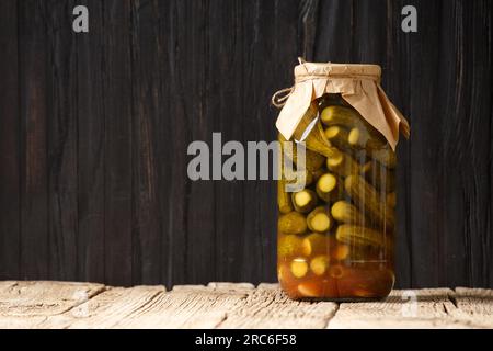 Eingelegte Gurken in einem geschlossenen Glasgefäß mit einem Deckel auf einer Holzfläche, dunklem Hintergrund, Kopierbereich. Stockfoto