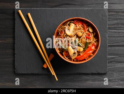 Teller mit Buchweizennudeln mit Gemüse, Pilzen, Hühnerfleisch, Draufsicht. Japanischer Soba in einer Tonschüssel und chinesische Essstäbchen Stockfoto