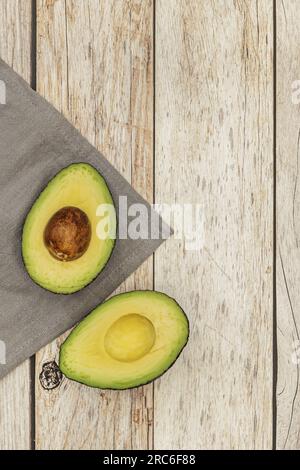 Eine reife Avocado, die auf einem grauen Tuch in zwei Hälften geschnitten wurde, und ein heller Holztisch Stockfoto