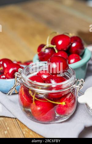 Einige reife Kirschen in Dosen in einem durchsichtigen Glasgefäß mit Deckel neben einem kleinen blauen Porzellan-Topf Stockfoto