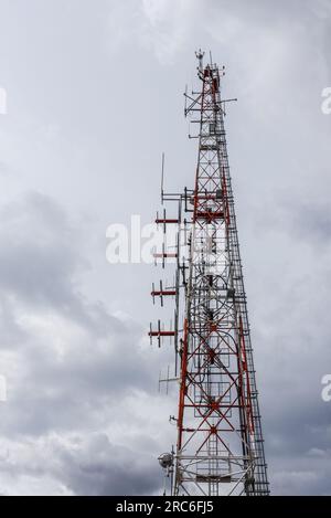 Ein hoher Telekommunikationsturm mit Antennen und einer Servicetreppe an einem Tag mit vielen Sturmwolken Stockfoto