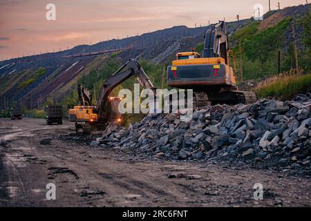 Hydraulikbagger und Kipplaster, die im Tagebau in Bergbau- und Verarbeitungsanlagen Erdbewegungsarbeiten durchführen. Stockfoto