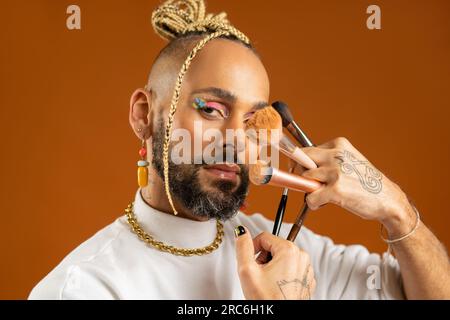 Afro-amerikanische Schwule mit leuchtendem Make-up und Make-up-Pinsel. Der hübsche Kerl trägt glänzendes Make-up. Modekonzept lgbtq. Männlicher Makeup-Künstler, Nahaufnahme Porträt Stockfoto