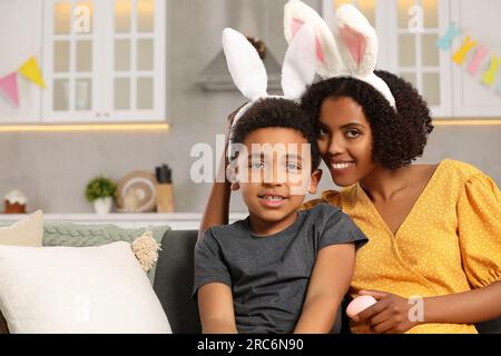 Fröhliche afroamerikanische Mutter und ihr süßer Sohn mit Hasenohren Stirnband drinnen. Osterfeier Stockfoto