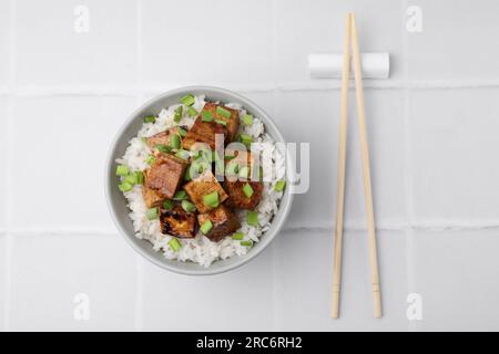 Schüssel mit Reis, gebratenem Tofu und Grün auf einem weiß gefliesten Tisch, flach liegend Stockfoto