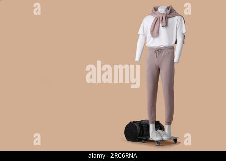 Männliche Puppe mit Turnschuhen und Tasche in weißem T-Shirt, Pullover und Hose auf beigefarbenem Hintergrund, Platz für Text Stockfoto