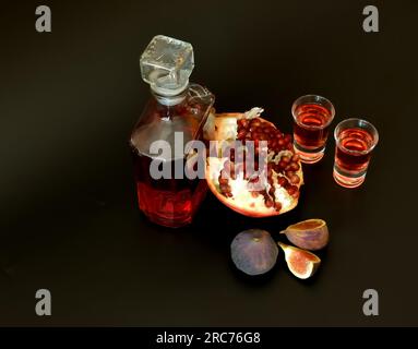 Feigen-Granatapfellikör auf schwarzem Hintergrund, eine Flasche und zwei Gläser Alkohol, reife Früchte in der Nähe. Draufsicht, flach liegend. Stockfoto