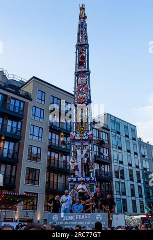 Brooklyn, New York, USA. 12. Juli 2023. Ein hoher Kirchturm mit Lilien und einer Band wird auf den Schultern von Gemeindemitgliedern getragen und im Rahmen des Fests unserer Lieben Frau vom Mount Carmel in Brooklyns Viertel Williamsburg durch die Gemeinde geführt. Der Kirchturm oder „giglio“ wird während des 11-tägigen Festes mehrmals auf der Straße hüpft oder „getanzt“, einschließlich dieses „Nachtlifts“. Kredit: Ed Lefkowicz/Alamy Live News Stockfoto