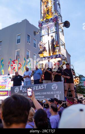 Brooklyn, New York, USA. 12. Juli 2023. Ein hoher Kirchturm mit Lilien und einer Band wird auf den Schultern von Gemeindemitgliedern getragen und im Rahmen des Fests unserer Lieben Frau vom Mount Carmel in Brooklyns Viertel Williamsburg durch die Gemeinde geführt. Der Kirchturm oder „giglio“ wird während des 11-tägigen Festes mehrmals auf der Straße hüpft oder „getanzt“, einschließlich dieses „Nachtlifts“. Kredit: Ed Lefkowicz/Alamy Live News Stockfoto