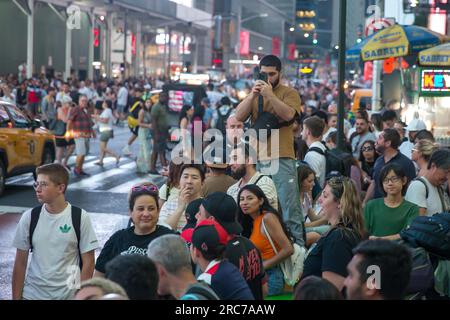 Die Menschen fotografieren den Sonnenuntergang an der 42. Street am Times Square an einem der vier Abende des Jahres, die als „Manhattanhenge“ bezeichnet werden, wenn die Sonne perfekt durch Räume zwischen Gebäuden des New York City Street Grid am 12. Juli 2023 in New York City gleitet. Tausende von Touristen und Einheimischen versammeln sich jedes Jahr für die Veranstaltung an Orten, die nach Westen über die Alleen blicken. Kredit: Brasilien Photo Press/Alamy Live News Stockfoto