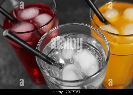 Gläser mit verschiedenen erfrischenden Mineralwasser mit Eiswürfeln und Strohhalmen auf grauem Tisch, Blick von oben Stockfoto