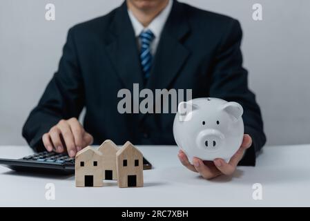 Geschäftsmann, der die Piggy Bank mit Home Calculator hält. Finanzinvestitionen und Spareinlagen, Management- und Buchhaltungskonzept. Stockfoto