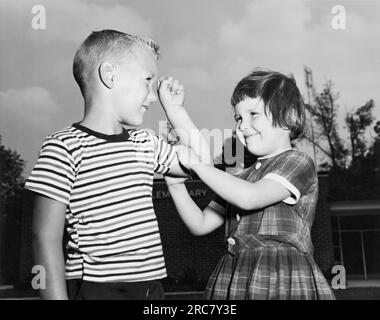 Maryland: 1965 Ein junges Mädchen Spürt den Bizepsmuskel eines Jungen. Sie sind im Kindergarten und beide nehmen am National School Lunch Program Teil, das von den USA verwaltet wird Veräußerung der Landwirtschaft. Stockfoto