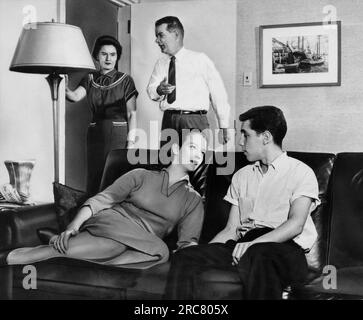 Massachusetts: September 1958 Ein Teenager-Paar, das auf einer Couch sitzt, blickt sich in die Augen, während die Eltern ihre Missbilligung zeigen. Stockfoto