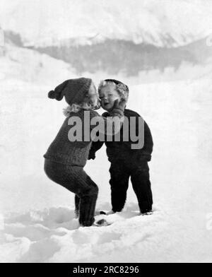 Vereinigte Staaten: c. 1922. Ein sehr junges Mädchen gibt ihrem kleinen Bruder im Schnee einen Kuss auf die Wange. Stockfoto