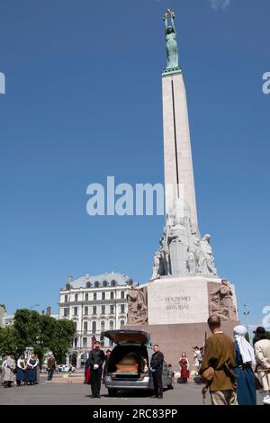 Gedenkfeier mit Leichenwagen am Freiheitsdenkmal in Riga mit Menschen in traditionellen lettischen Kostümen. Das Denkmal ehrt Soldaten, die gestorben sind Stockfoto