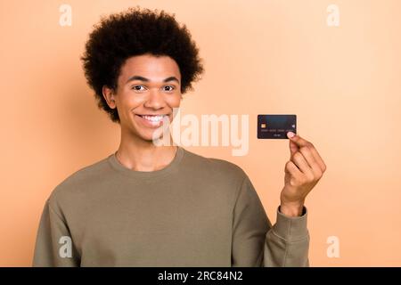 Porträtfoto von attraktivem jungen Promoter Typ witzig Chevelure Kleidung Sweatshirt halten Debitkarte billig einkaufen isoliert auf beigefarbenem Hintergrund Stockfoto