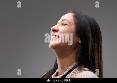 Junge Frau mit langen Haaren, die ihre Freude unterdrückt, blickt nach oben und links. Sie sieht sich eine glänzende Zukunft vor. Profilbild einer philippinischen Dame in beiger Bluse Stockfoto