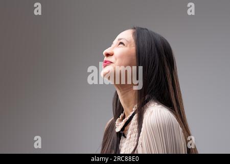 Ein Profilbild einer freudigen Filipino-Frau mit langen Haaren, die nach links blickt. In einer beigen Bluse mit schwarzer Schleife sieht sie sich ein Versprechen aus Stockfoto