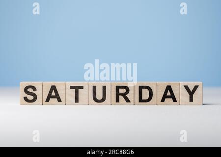 Text Samstag auf Holzwürfeln auf blauem Hintergrund. Wochentag auf Holzblöcken. Webbanner für Wochentage. Ursprünglicher Kalender. Teil der Serie. Zeitkonzept Stockfoto