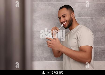 Glücklicher Mann, der sein Smartphone benutzt, während er im Badezimmer Zähne putzt. Internetsucht Stockfoto