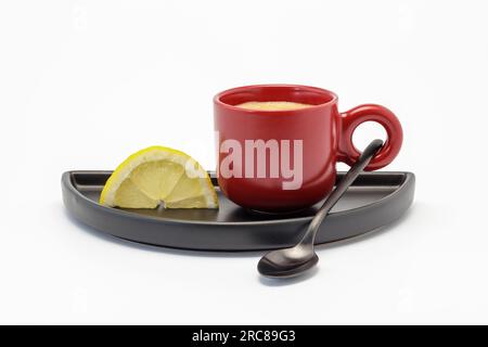 Rote Tasse gefüllt mit starkem Kaffee und ein Stück Zitronenausschnitt, natürliches Kopfschmerzmittel Stockfoto