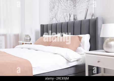 Komfortables Bett und Lampen auf Nachttischen im hellen Zimmer. Stilvolle Innenausstattung Stockfoto